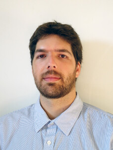 Porträt von Celso Fornari mit dunklem Haar und Bart vor grauem Hintergrund.